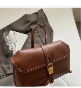 Detail of vintage brown leather handbag with metallic clasp and stitching on white bedding