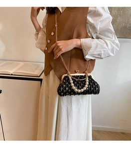 Detail of black pleated shell bag with gold floral patterns and pearl top handle strap