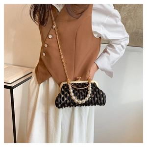 Detail of black pleated shell bag featuring pearl handle and gold chain strap