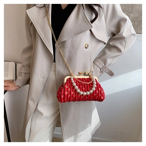Detail of red pleated clutch bag featuring pearl handle and gold chain strap on a model