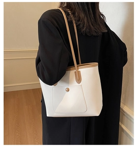 Detail of white tote bag with brown leather trim and pocket shown on a model's shoulder