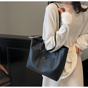 Detail of minimalist black tote bag with textured leather surface and shoulder strap