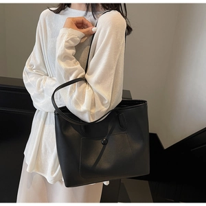Detail shot of the matte black tote bag showing the front pocket and round buckle hardware
