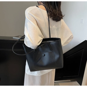 Close-up of a large black leather tote bag featuring a front pocket and long shoulder straps