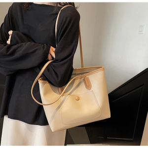 Detailed view of large cream tote bag with brown trim on a model in minimalist setting