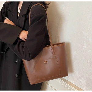 Detail of dark brown leather tote bag with front pocket shown on a black blazer