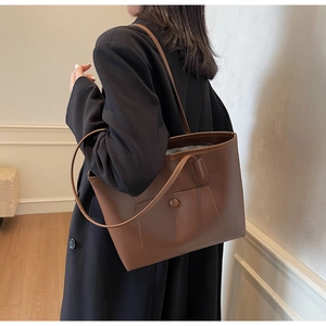 Brown leather tote bag featuring a front pocket shown on a model in soft indoor lighting