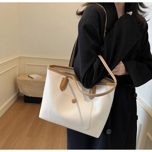 Detail of white leather tote bag with brown trim carried by model in a minimalist room
