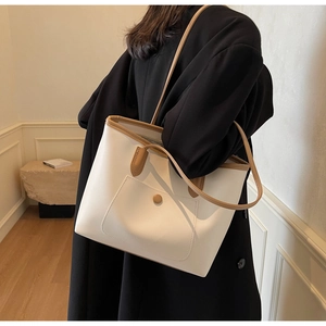 Detail view of a large cream tote bag with brown leather trim and front buckle pocket
