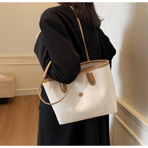 Detail of a large cream tote bag with brown straps and a front pocket on a model's shoulder