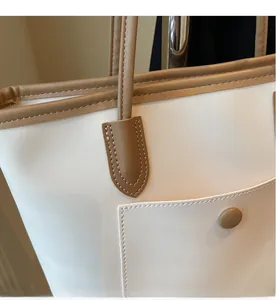 Detail of a large tote bag showing white canvas and brown leather stitching with pocket