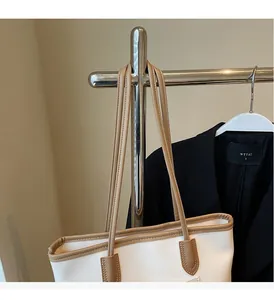 Detail of white leather tote bag with brown straps and fine stitching on a hanger
