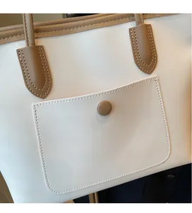 Detail of two-tone tote bag featuring white leather texture and brown stitched pocket