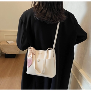 Detailansicht der cremeweißen Leder-Eimertasche mit Seidenschal und Metall-Druckknopf