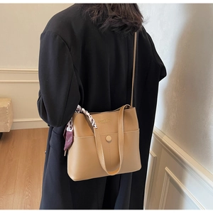 Detail der hellbraunen Beuteltasche mit dekorativem Seidentuch und goldener Logoprägung