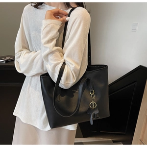 Detail of a large black PU leather tote bag with a decorative elephant pendant on the strap