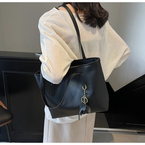 Detail view of large black leather tote bag featuring a decorative elephant charm