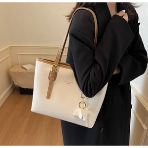 Detail view of large white tote bag with brown straps and elephant charm on shoulder