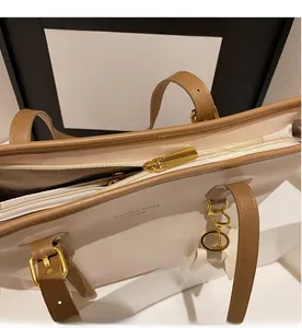 Close-up of golden metal zipper and brown leather trim on a beige tote shoulder bag
