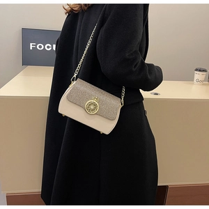 Dettaglio della borsa beige con catena e fibbia dorata con patta a trama metallica