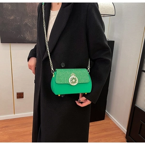 Dettaglio borsa a tracolla verde con chiusura a corona dorata su cappotto nero