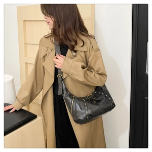 Detail of a vintage black crescent bag with gold studs and wide strap on trench coat