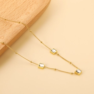 Gold beaded necklace featuring three square crystal pendants on a soft beige background