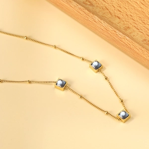 Golden bead necklace with three square gray gemstone pendants on a warm beige background