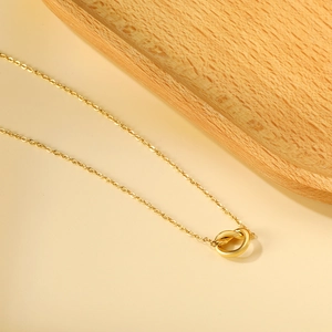 Detail of 18K gold plated knot pendant necklace on a minimalist wooden tray backdrop