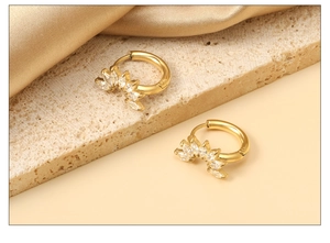 Détail de boucles d'oreilles pétales dorées avec zircons marquises sur surface en pierre