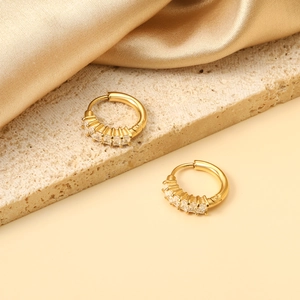 Détail de boucles d'oreilles huggie dorées avec diamants sur un tissu en soie élégant