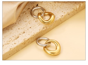 Détails de boucles d'oreilles bicolores avec pendentifs dorés sur une pierre beige