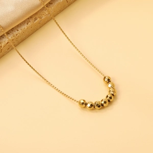 Detail of gold beaded pendant necklace on textured stone and satin fabric