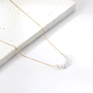 Elegant gold stainless steel necklace with six white pearls on white display stand