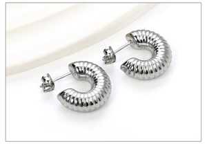 Détail des boucles d'oreilles créoles C argentées avec motif de métal côtelé torsadé