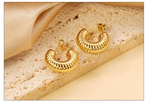 Détail de boucles d'oreilles créoles dorées torsadées avec texture sur pierre et soie