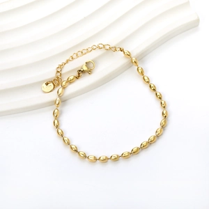 Polished golden stainless steel wheat bead bracelet on a minimalist white display stand