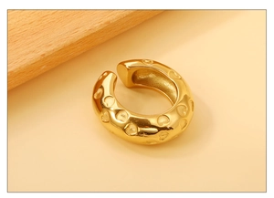 Détail du ear cuff en C plaqué or 18K avec motifs de cœurs gravés sur bloc de bois