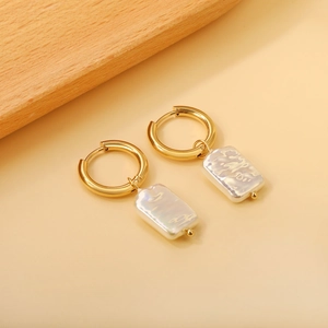 Elegant gold hoop earrings with rectangular white baroque pearl pendants on beige background