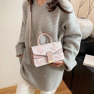 Sac bandoulière rose avec broderie florale et poignée tressée dans un décor d'intérieur