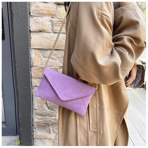 Detail of purple faux suede envelope bag with elegant gold chain strap worn on coat