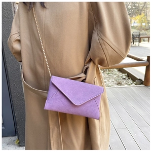 Detail of purple faux suede envelope bag with elegant gold chain strap on a long coat