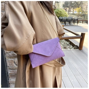 Detail of purple faux suede envelope bag featuring a minimalist gold chain strap