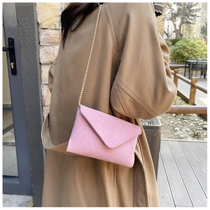Pink suede envelope crossbody bag featuring a delicate gold chain strap on a model