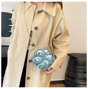 Detail of sky blue flower-shaped crossbody bag with gold chain strap on model coat