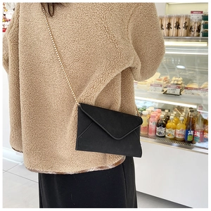 Model wearing a black matte envelope crossbody bag with a slim gold chain shoulder strap