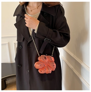 Detailed view of flower-shaped orange crossbody bag with gold chain strap on black coat