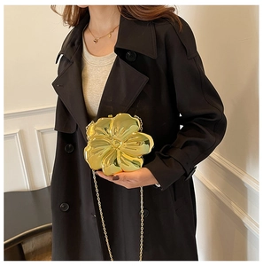 Detailed close-up of a golden flower-shaped metal clutch bag with chain strap on a model