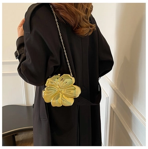 Detail of a metallic gold flower chain bag worn over a black coat on a model