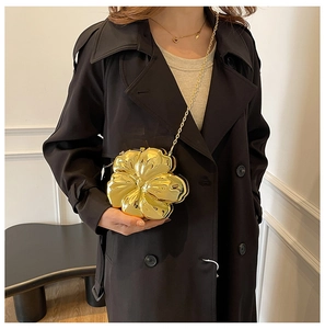Close-up of golden petal-shaped crossbody bag with metal chain on a black trench coat